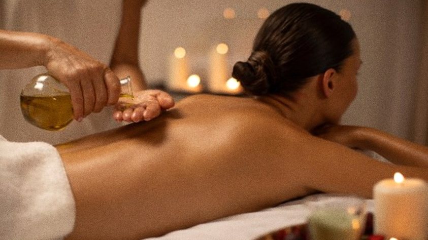 Huile versée sur le dos d'une femme allongée, à la lueur de bougies, massage Californien de Biostem