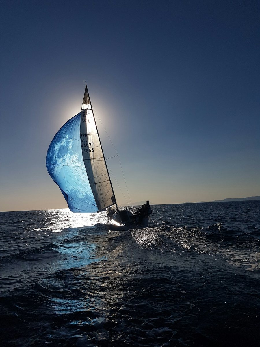 Voilier sous spinnaker bleu, à contre-jour sur une mer sombre