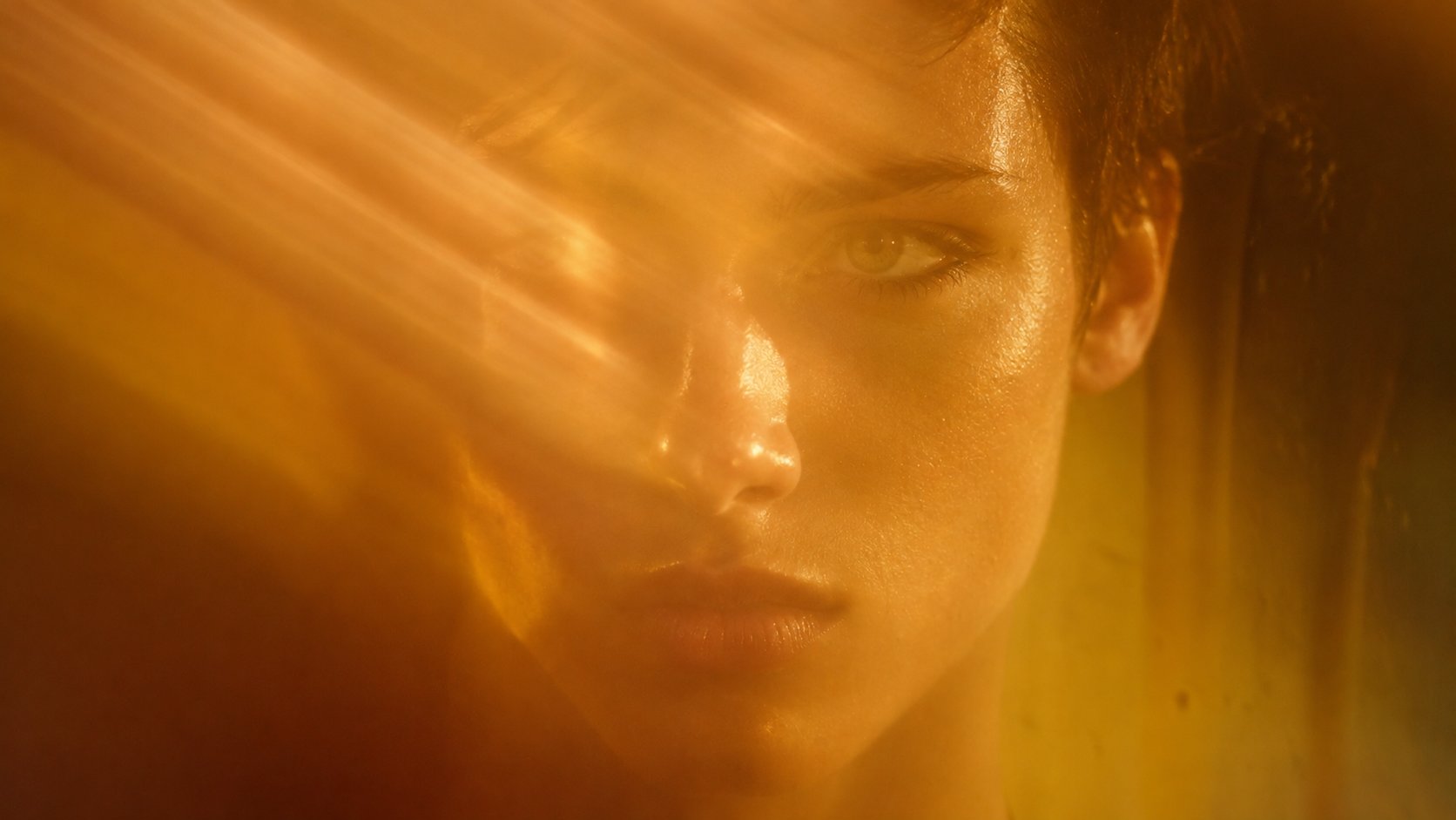 Visage de femme aux cheveux courts traversé de rayons de lumière orangée et dorée