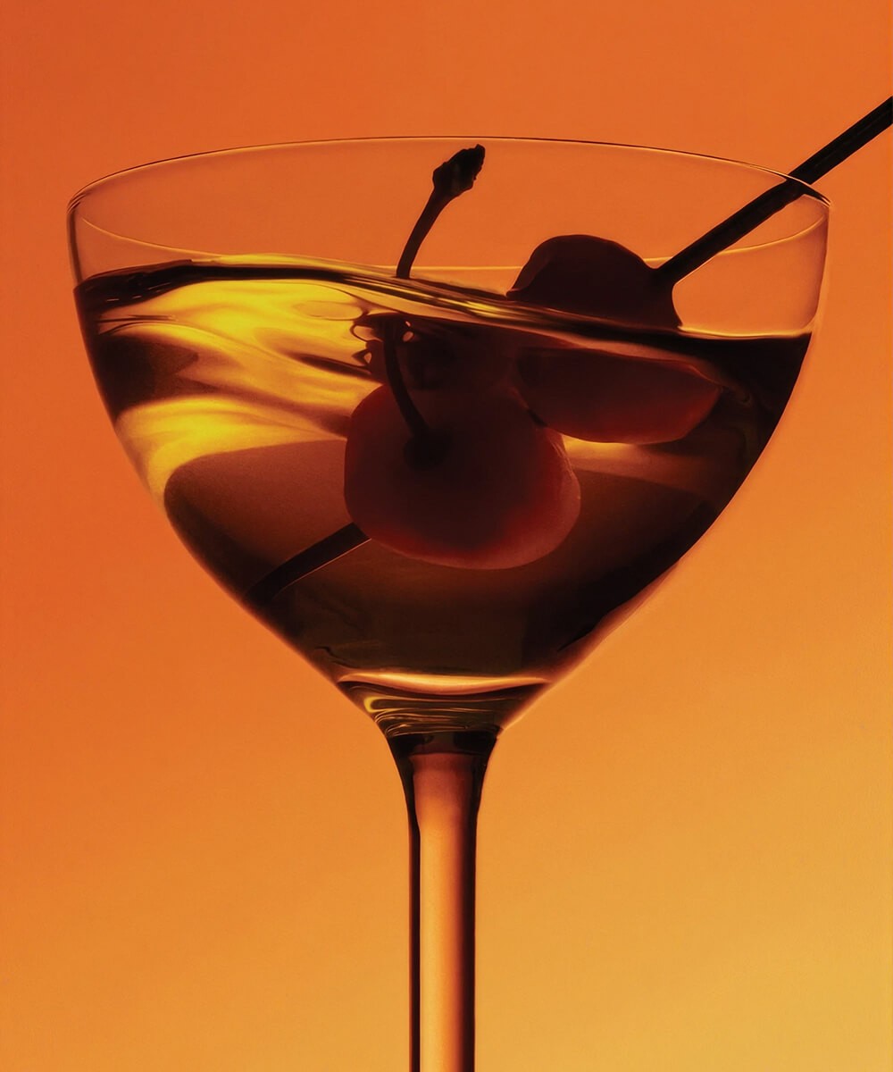 Cocktail ambré avec cerises dans un verre à pied, sur fond orange, visuel de survol du projet Winston Canopy Foundation
