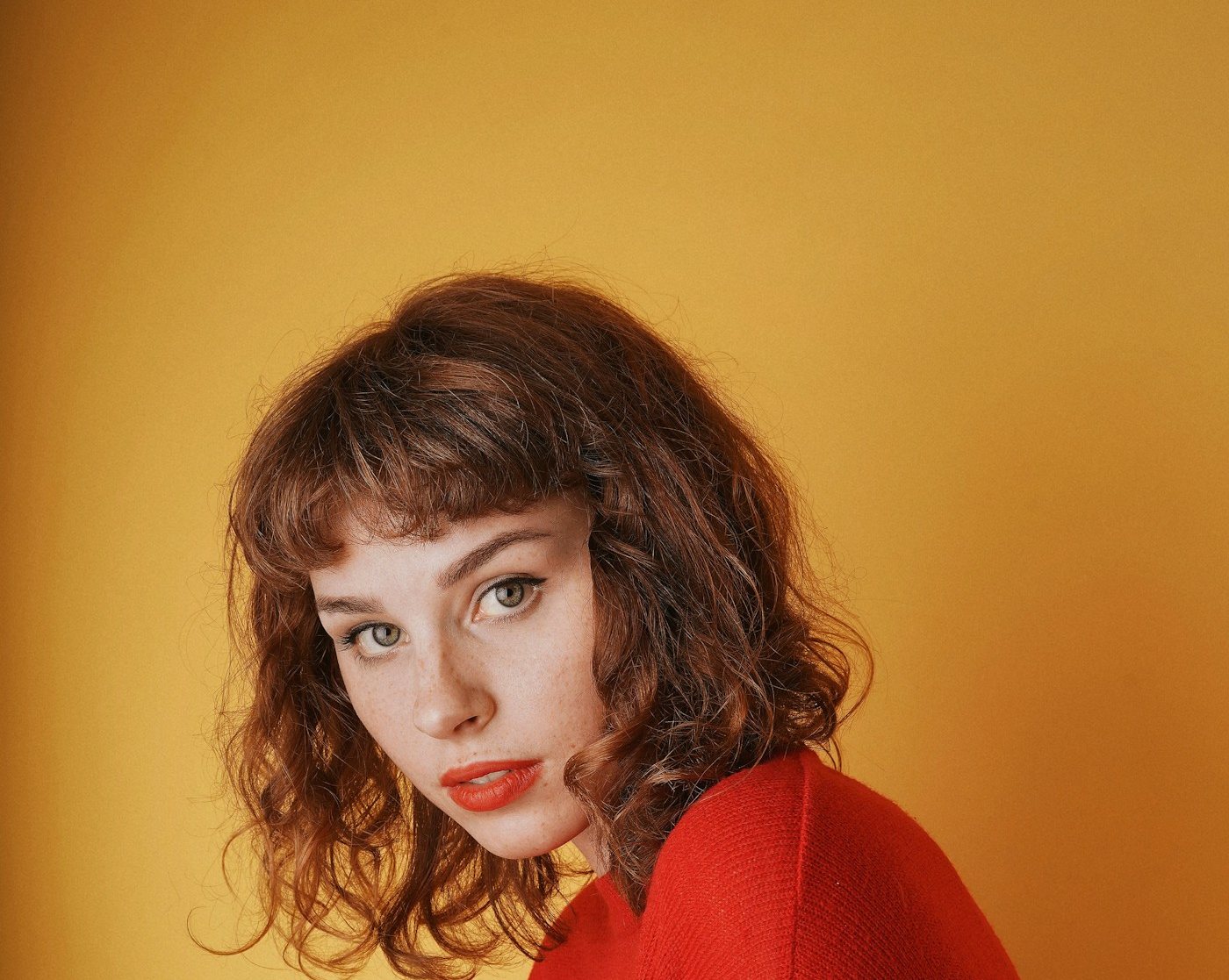 Portrait d'une femme aux cheveux bouclés en pull rouge sur fond ocre, réalisation Studio 47